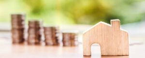 Kleines Holzhäusschen vor aufgestapelten Münzen als Visualisierung für die Immobilienbewertung